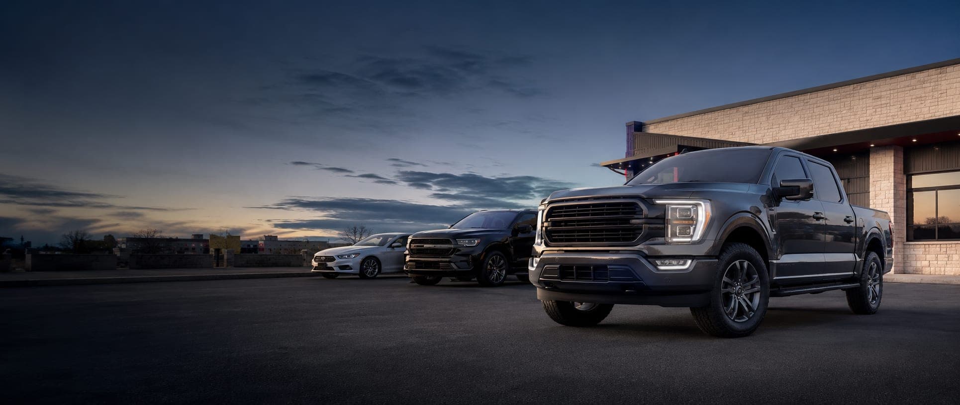Trucks, SUVs, and cars lined up at dusk at Cowtown Auto Group in Fort Worth